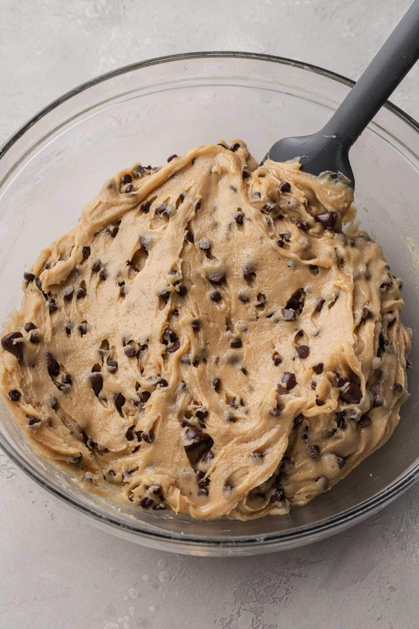 Un tazón de vidrio lleno con la masa de galleta con chispas de chocolate terminada.