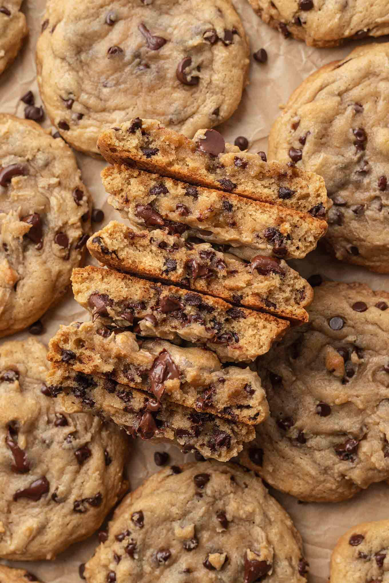 Una vista aérea de varias galletas con chispas de chocolate sobre un trozo de papel pergamino marrón.  Tres de las galletas se parten por la mitad para mostrar la textura.