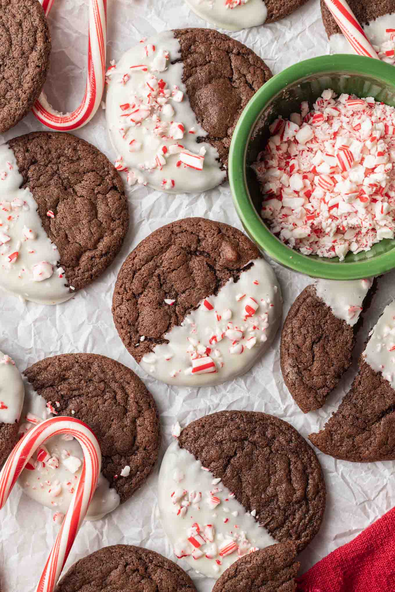 Una vista aérea de galletas de chocolate y menta bañadas en chocolate blanco, con un plato de bastones de caramelo triturados. 