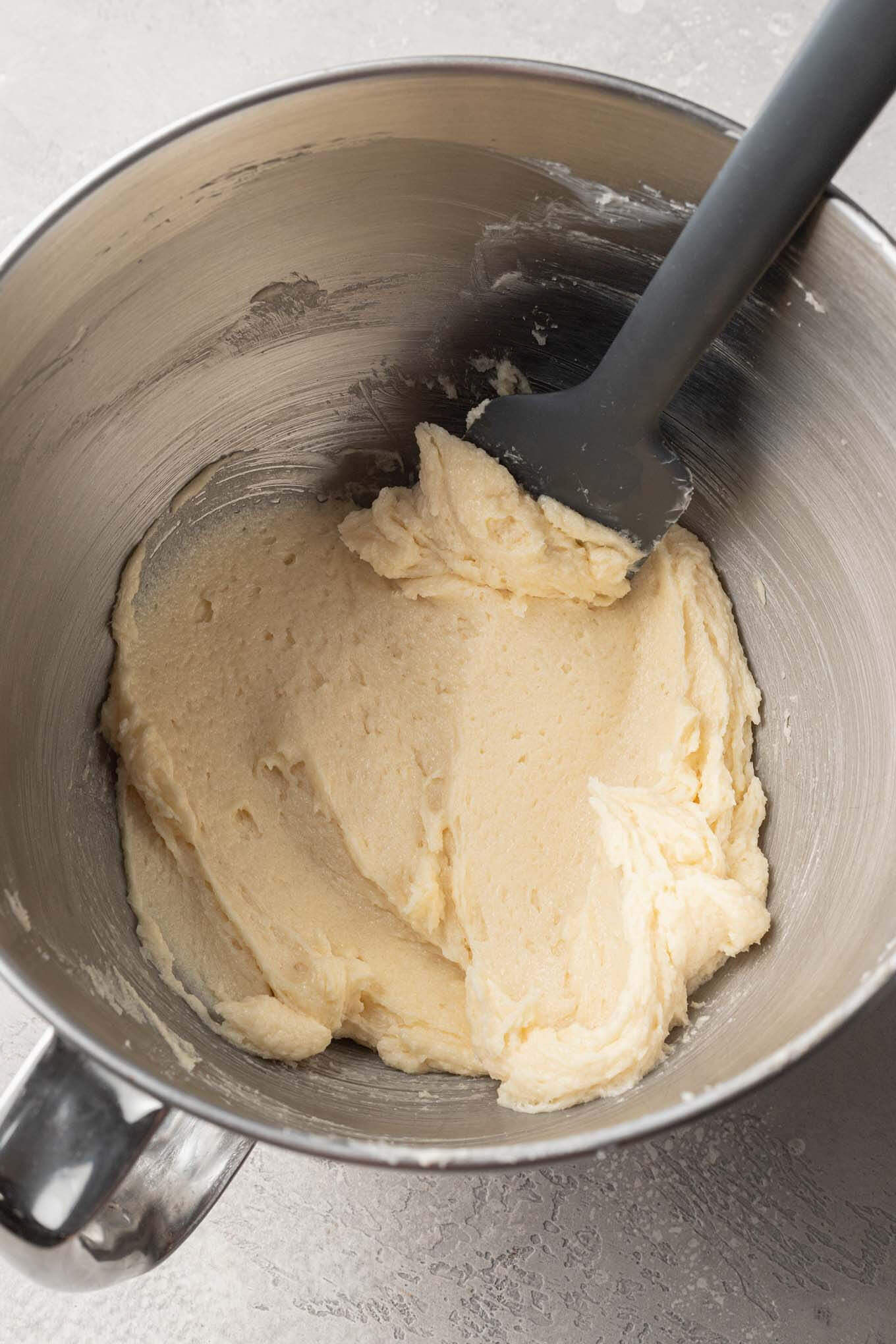 Una vista aérea de los ingredientes húmedos necesarios para las galletas de azúcar en un tazón, con una espátula de goma.  