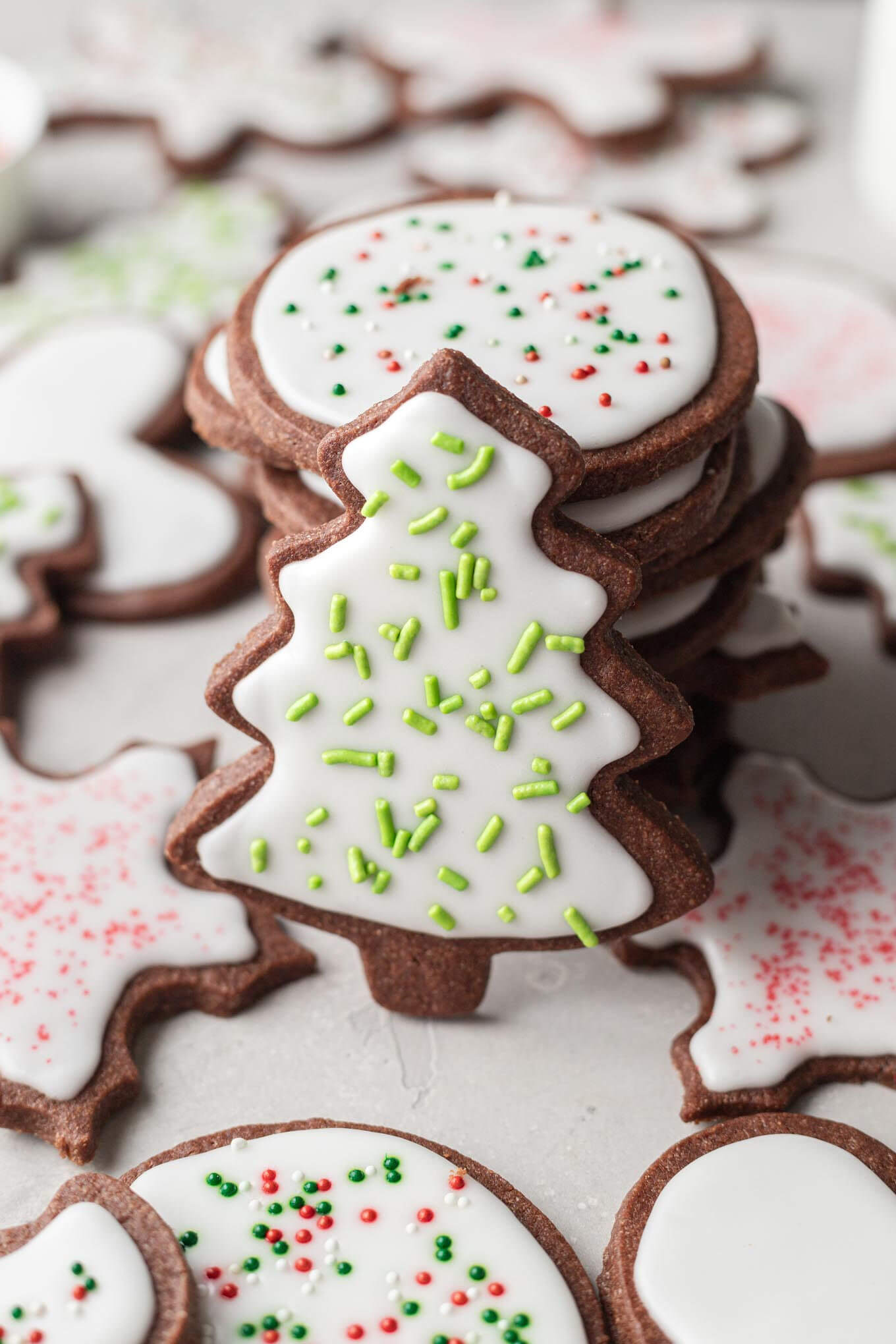 Una pila de galletas de chocolate y azúcar, decoradas con glaseado y chispas.  Una galleta con forma de árbol se apoya contra la pila. 