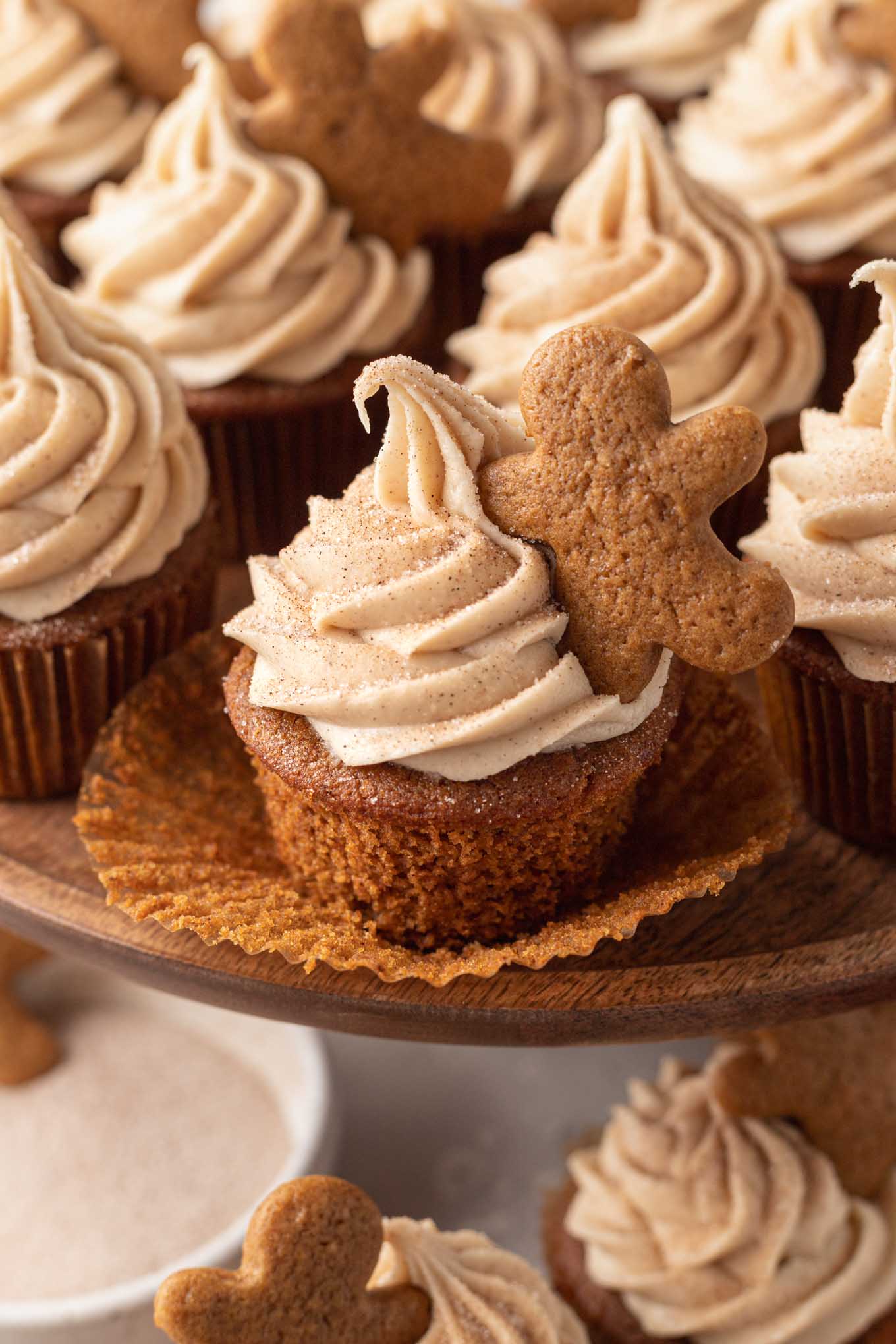 Un cupcake de pan de jengibre con el molde para cupcakes bajado.  Detrás hay más cupcakes en un puesto de pasteles. 