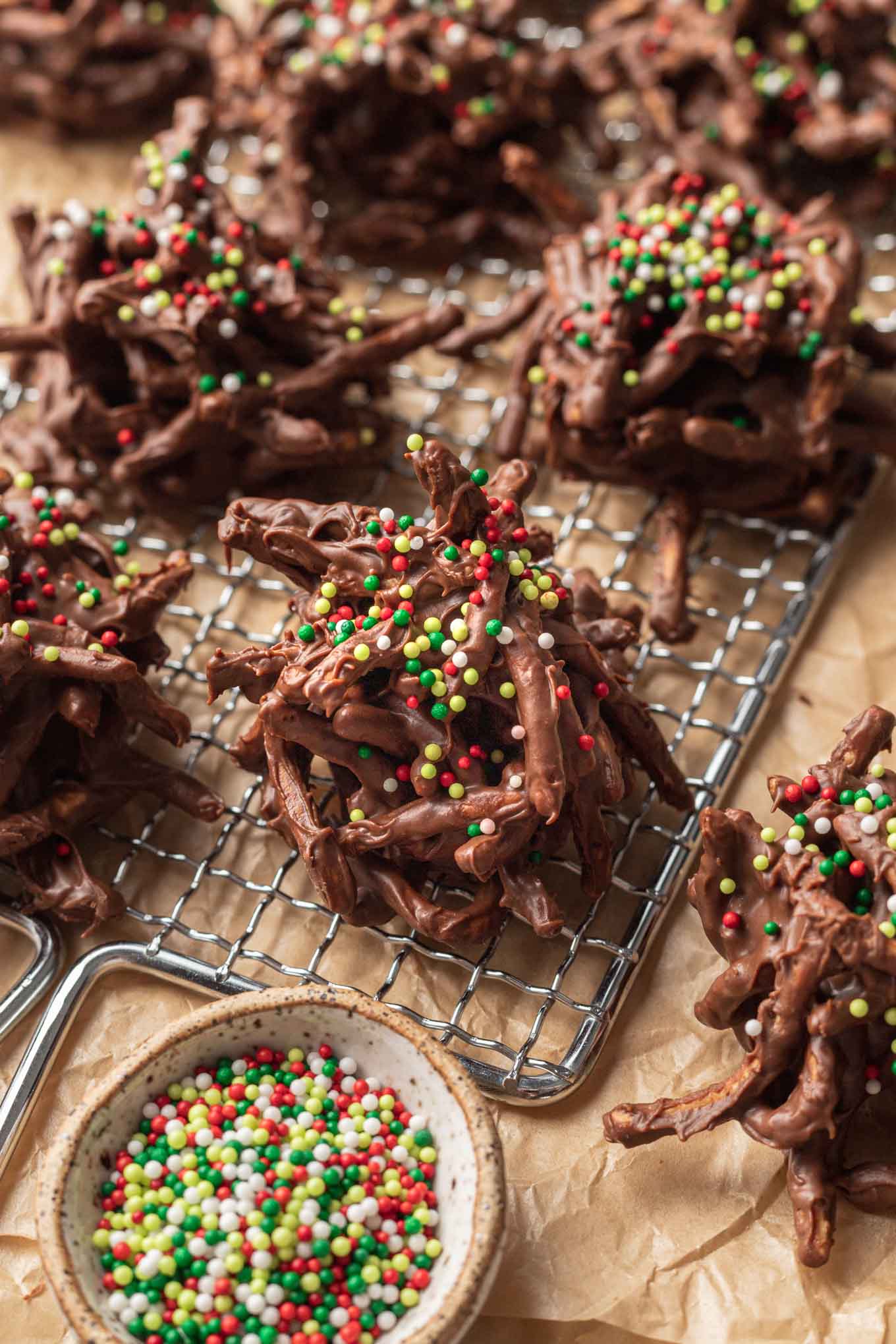 Galletas de chocolate en forma de pajar sobre una rejilla, colocadas sobre papel pergamino. 