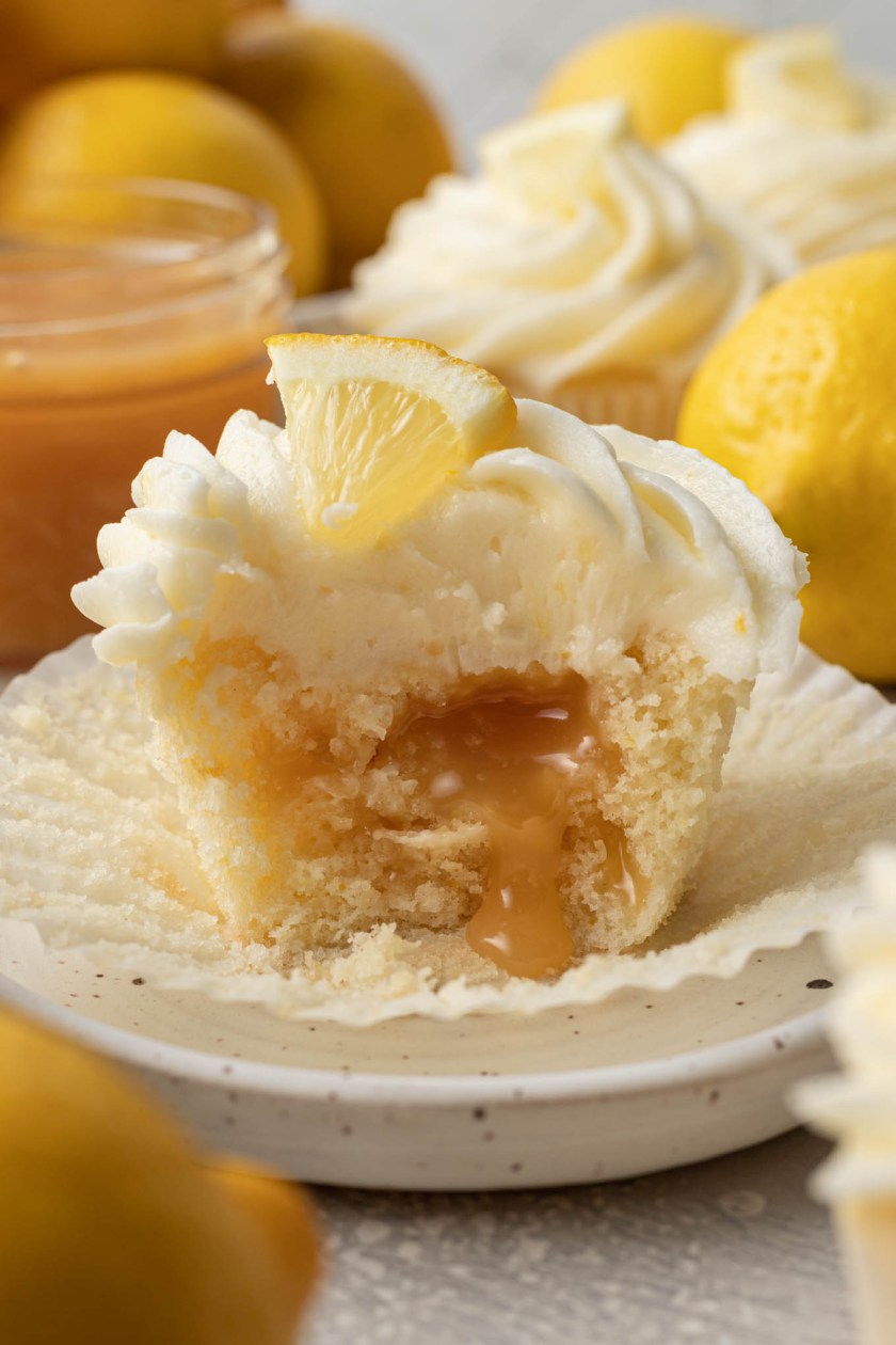 Una vista de cerca de un cupcake relleno de cuajada de limón al que le falta un bocado. La cuajada de limón rezuma del pastelito.
