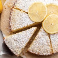 Una tarta de aceite de oliva cortada en rodajas sobre un trozo de papel de horno.  Una vez retirada la rodaja.