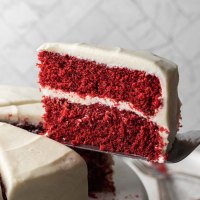 Una torta di velluto rosso a fette su un'alzatina. La fetta di torta viene sollevata per mostrare la consistenza della torta.