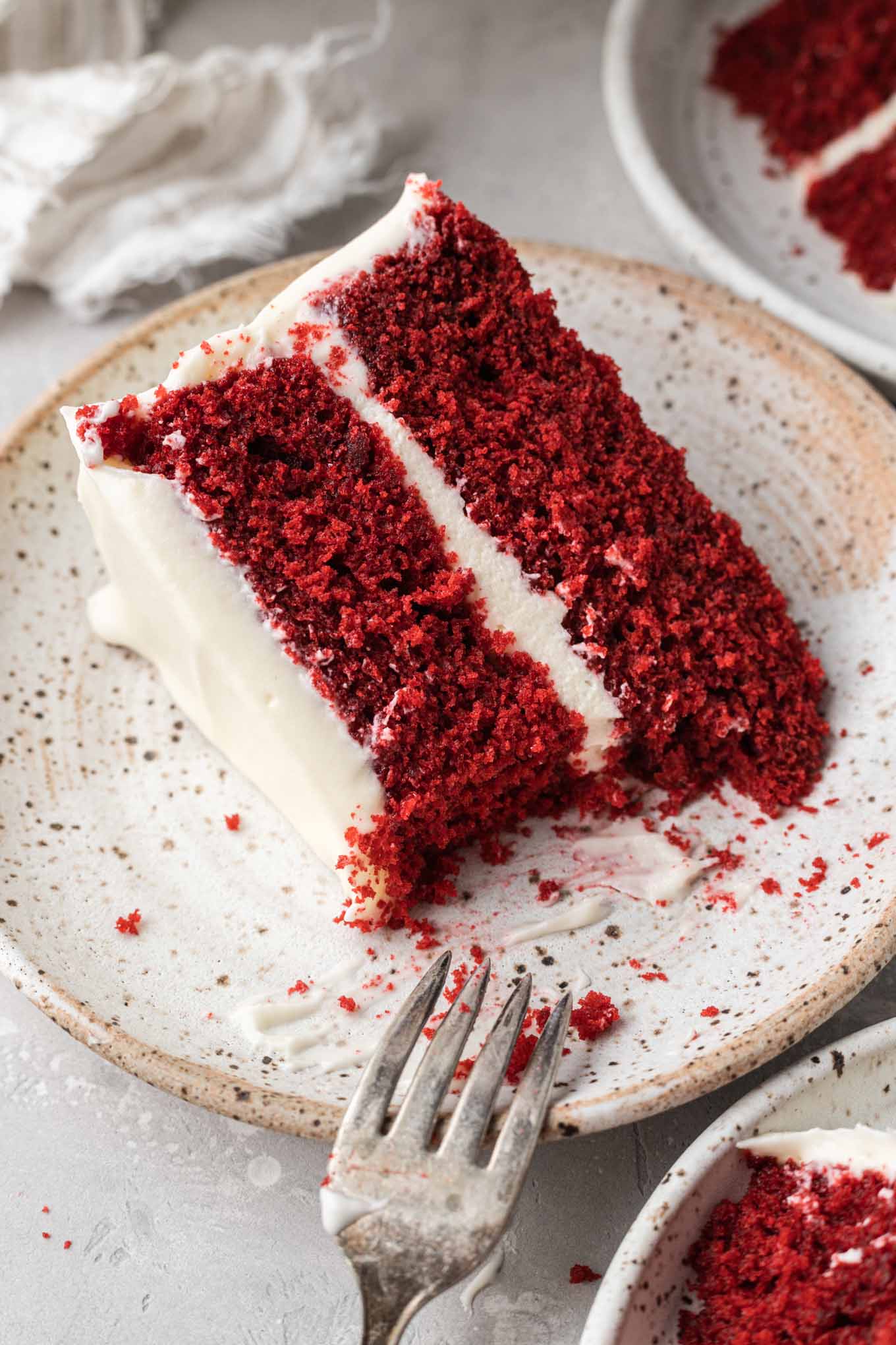Una fetta di torta di velluto rosso glassato su un piatto bianco maculato. 