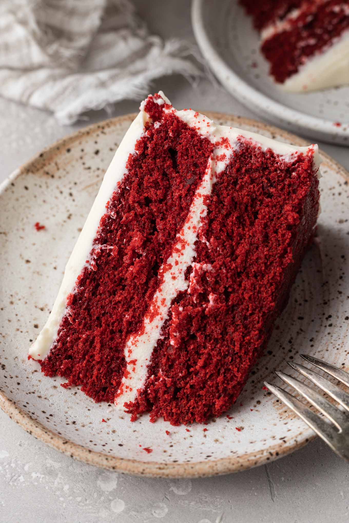 Una fetta di torta di velluto rosso glassato su un piatto da dessert maculato. 