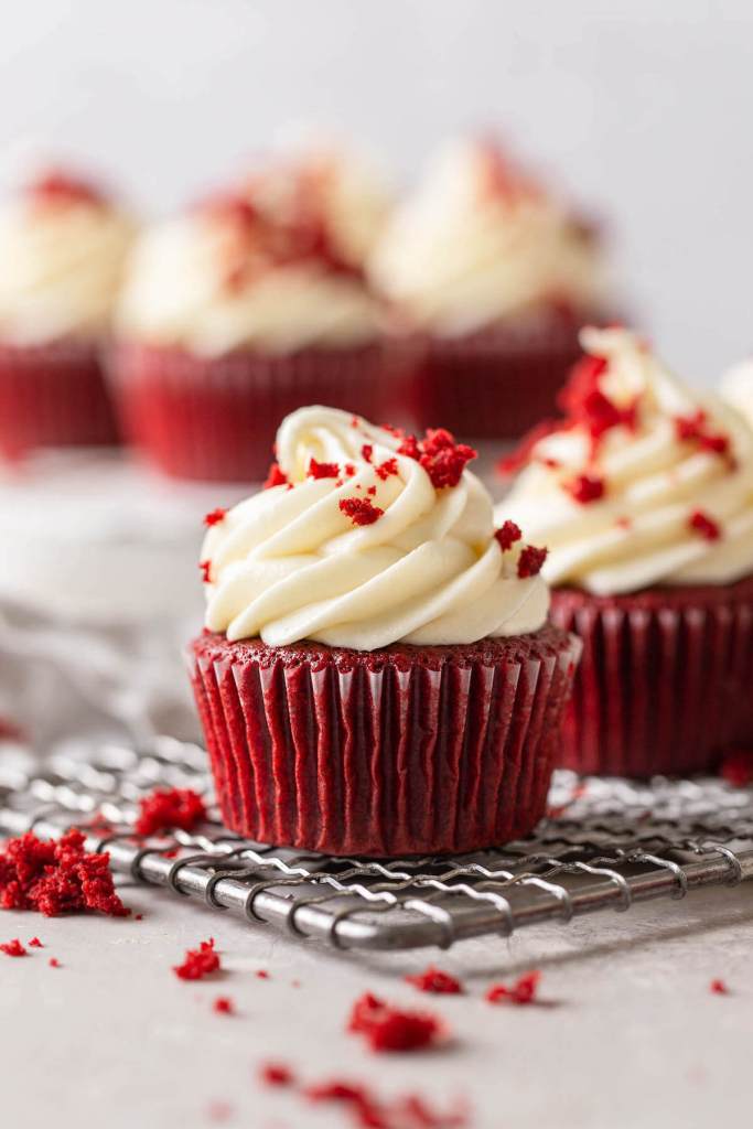 Una vista lateral de cupcakes de terciopelo rojo esmerilado sobre una rejilla de alambre para enfriar. 