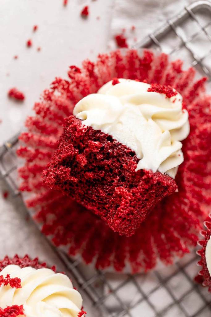 Una vista aérea de un cupcake de terciopelo rojo tumbado de lado.  Falta un bocado. 