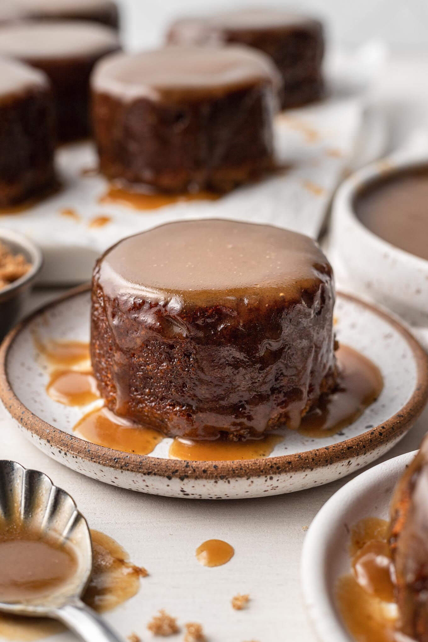 Un pudín de caramelo pegajoso en un plato moteado.  Más descanso en el fondo. 