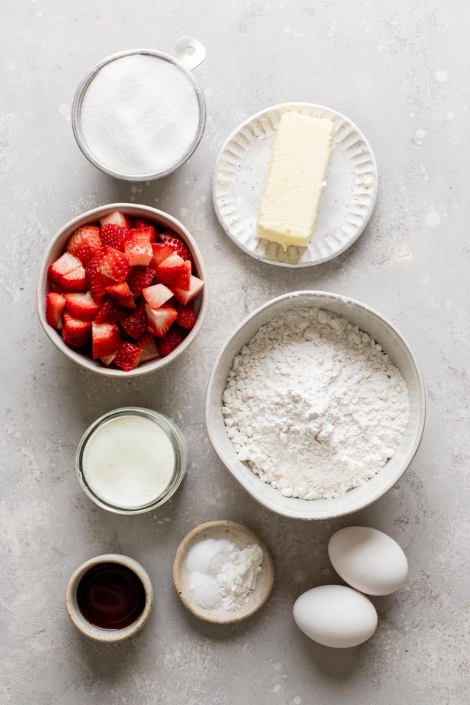 Una vista aérea de los ingredientes necesarios para hacer cupcakes de fresa y glaseado de fresa. 