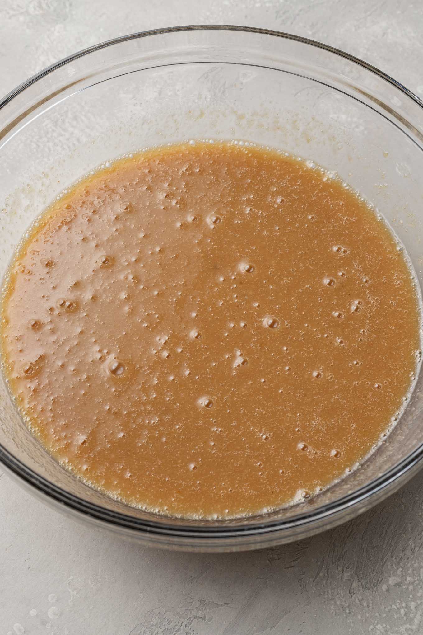 Una vista aérea de los ingredientes húmedos para el pastel de puré de manzana, en un tazón de vidrio. 