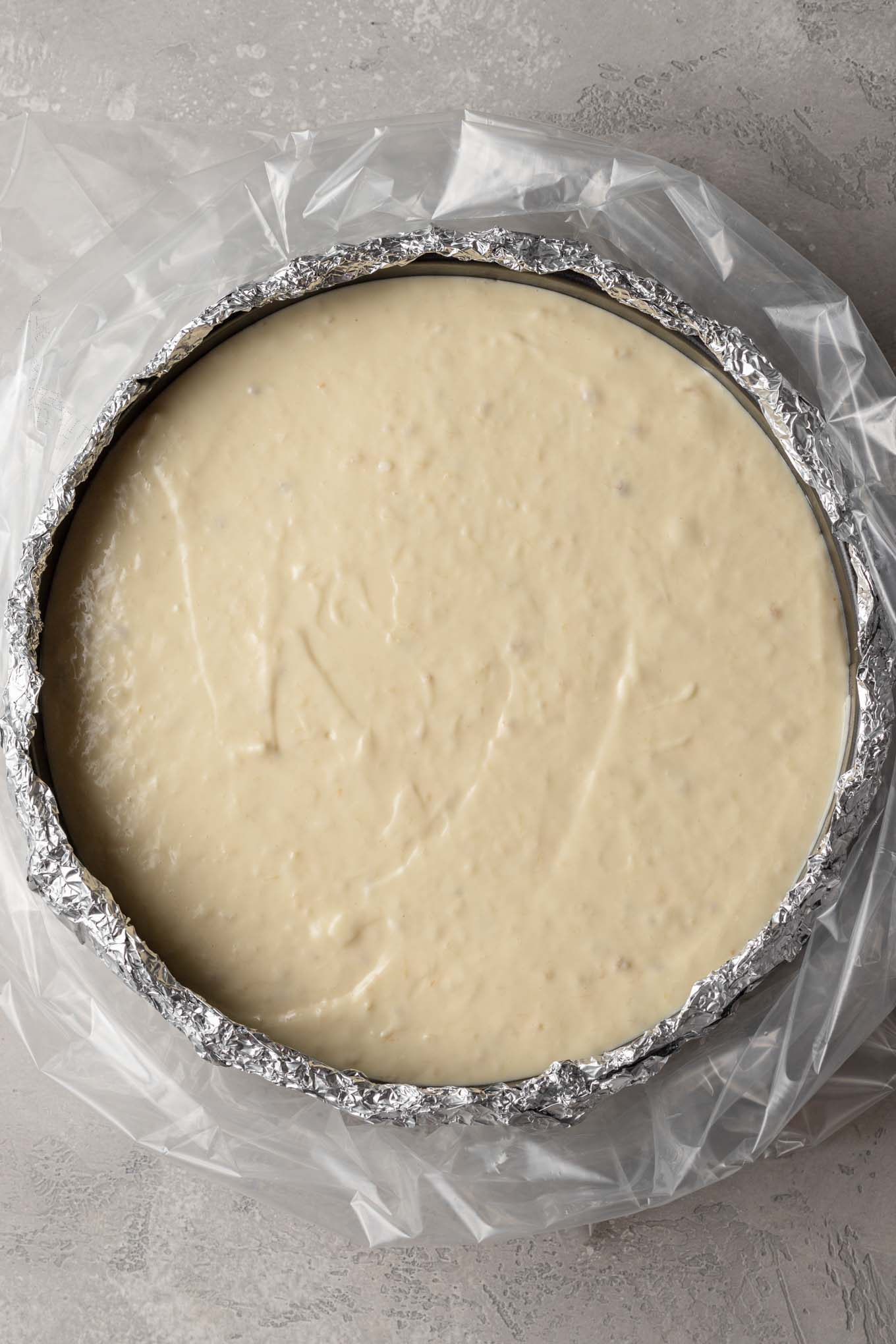 Una vista aérea de una tarta de queso sin hornear.  La sartén se envuelve en papel de aluminio y se coloca en una bolsa para horno. 