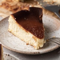 Un trozo de tarta de queso vasca sobre un plato moteado de blanco.  Hay un tenedor apoyado sobre el plato.