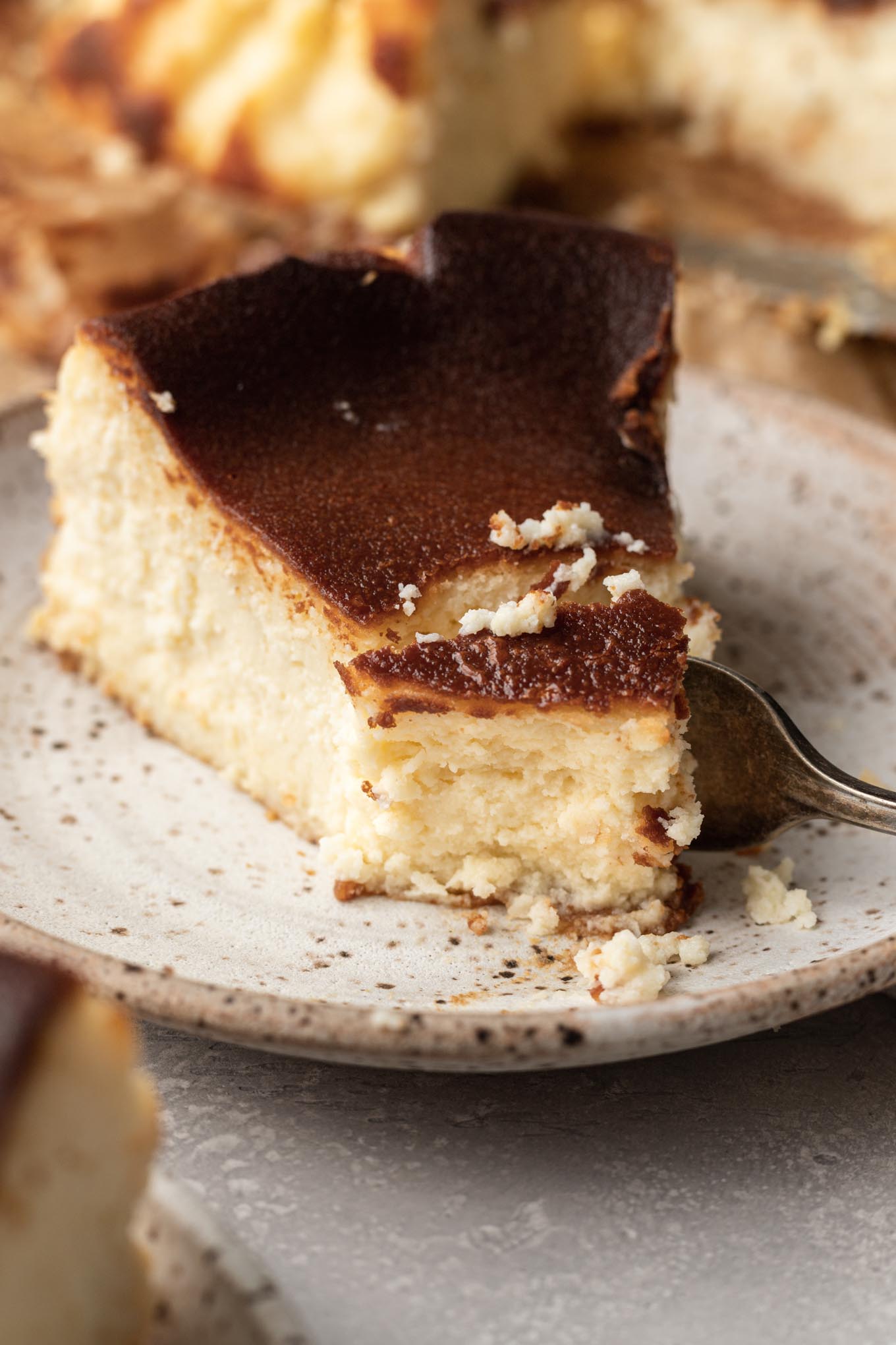 Un trozo de tarta de queso vasca quemada, con un tenedor cortando un trozo del extremo. 