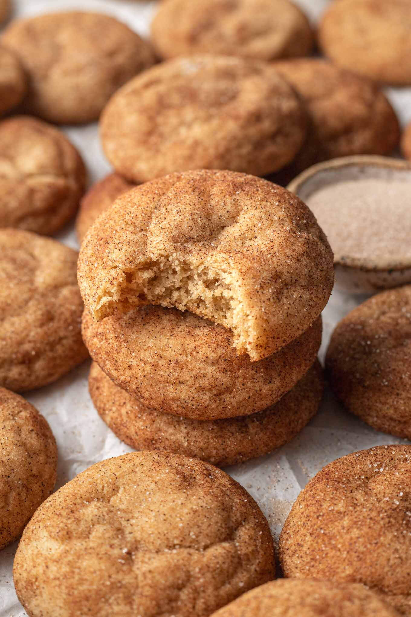 Una pila de tres snickerdoodles de mantequilla marrón, rodeados de más galletas. 