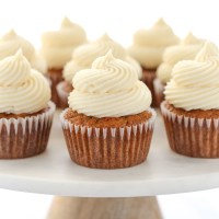 Un grupo de cupcakes de pastel de zanahoria cubiertos con glaseado de queso crema sobre un soporte de pastel de mármol.