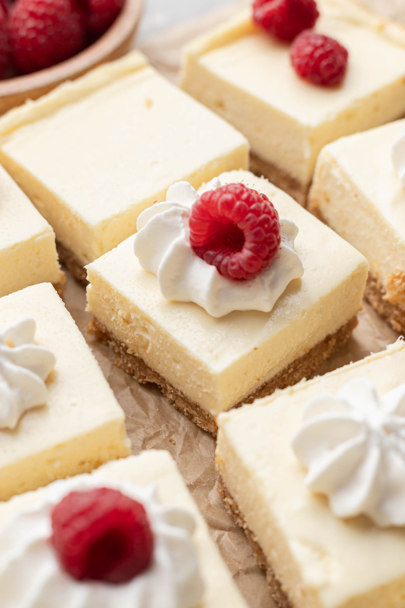 Barras de tarta de queso en rodajas cubiertas con crema batida y frambuesas frescas. 