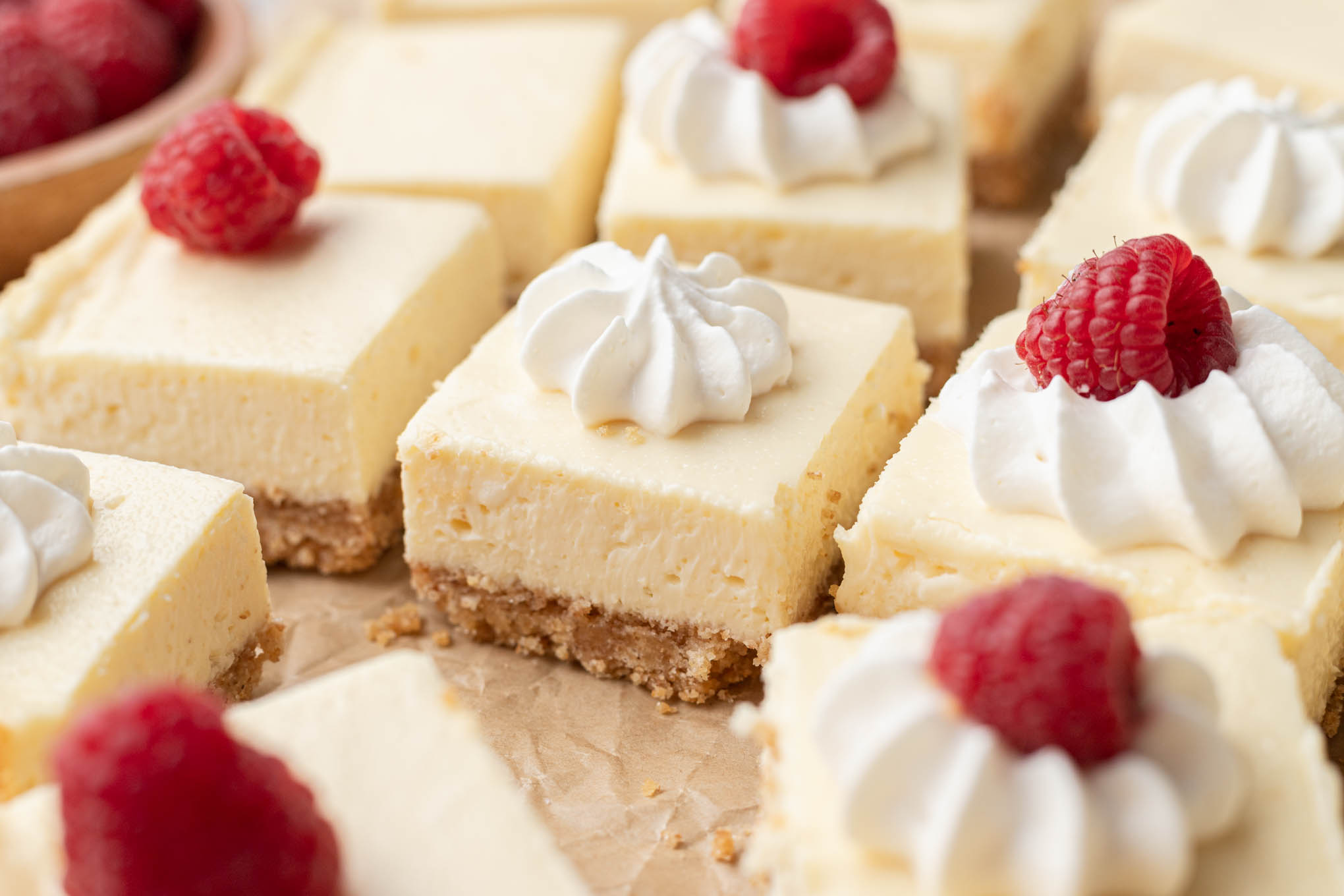 Varias barras de tarta de queso cubiertas con crema batida y frambuesa fresca.