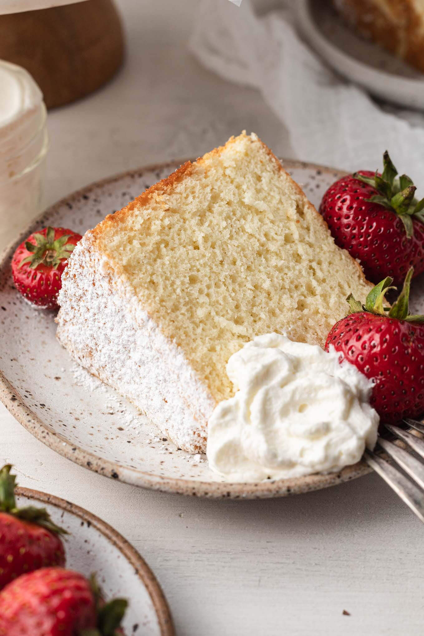 Un trozo de pastel de gasa sobre un plato moteado de blanco.  El plato se adorna con fresas frescas y una cucharada de nata montada.