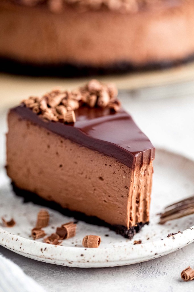 A slice of chocolate cheesecake with a bite missing on a white speckled plate. 