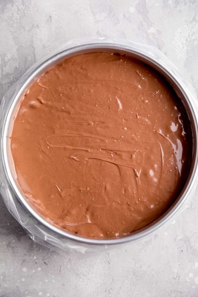 An overhead view of an unbaked chocolate cheesecake in a springform pan that's been placed in an oven bag.