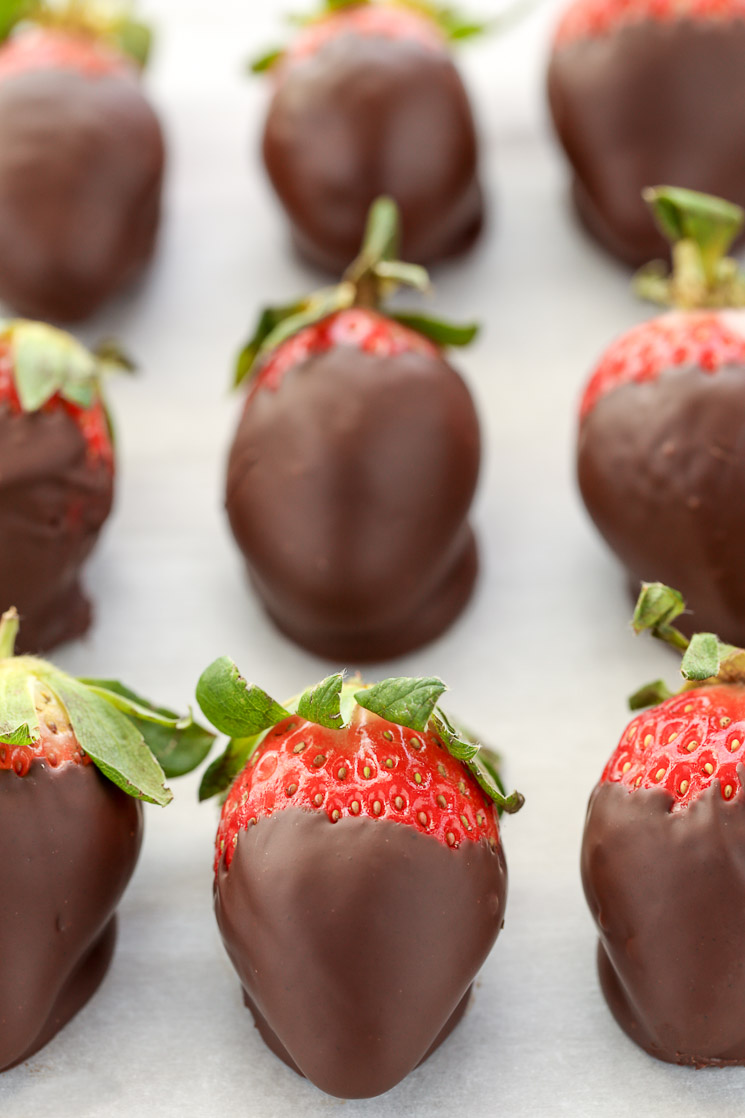 Fresas cubiertas de chocolate alineadas sobre un trozo de papel pergamino.