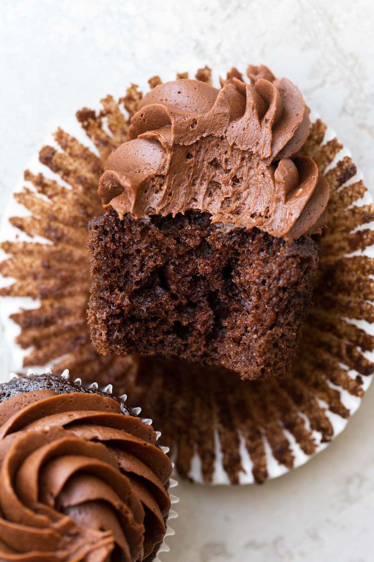 Un cupcake de chocolate de lado al que se le ha quitado un bocado para mostrar la textura del pastel y el glaseado.