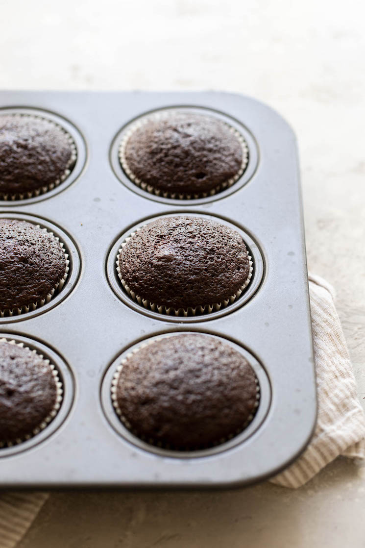 Un molde para muffins que contiene pastelitos horneados sobre una superficie rústica.