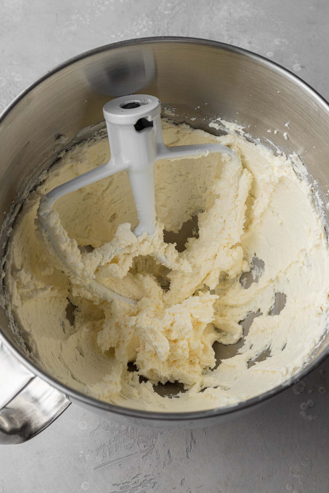 Una vista aérea de crema de mantequilla y queso crema en un tazón para mezclar, con un accesorio de paleta apoyado en el interior. 