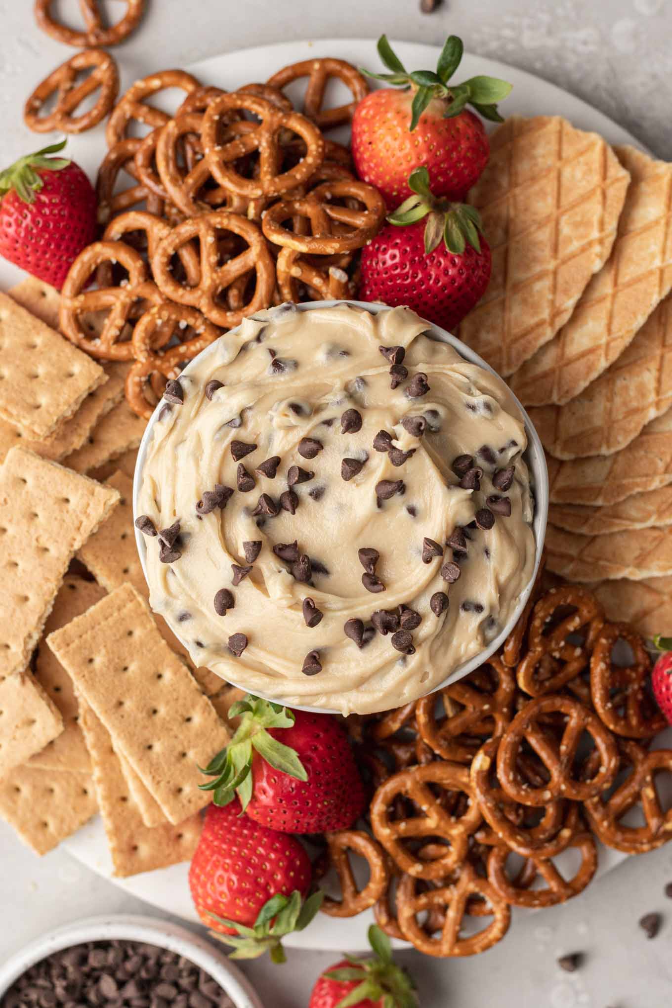 Una vista aérea de un plato de masa para galletas con chispas de chocolate en un plato con pretzels, galletas Graham y bayas. 