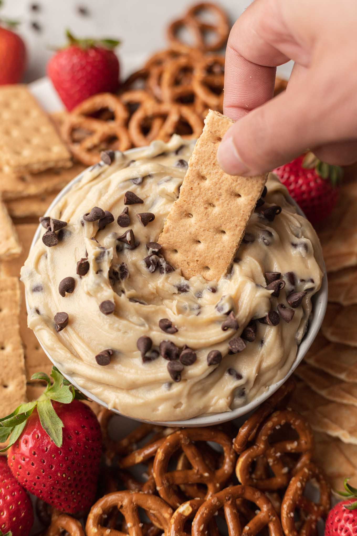 Una galleta Graham sumergida en salsa de masa para galletas con chispas de chocolate, que descansa sobre un plato. 