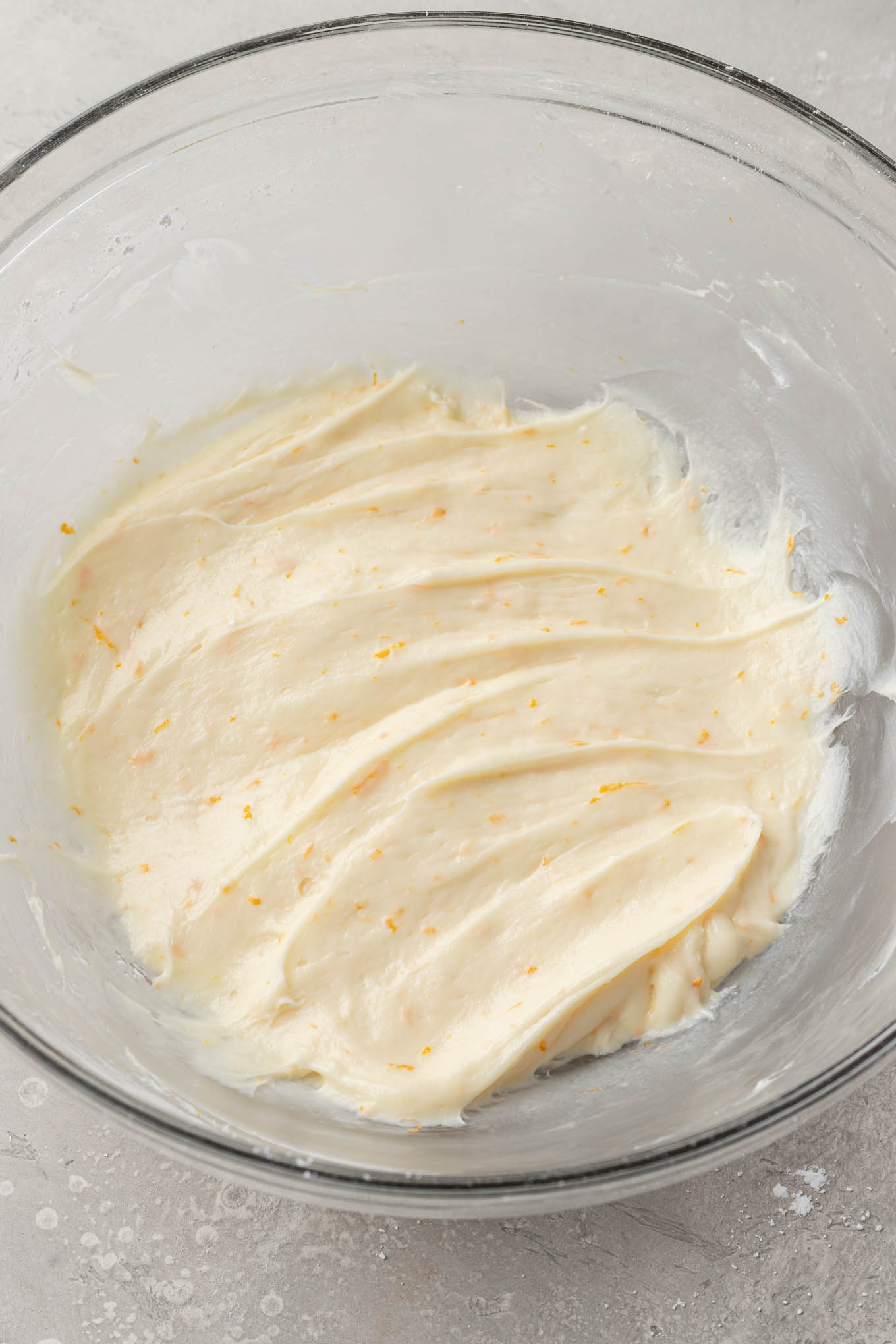 Una vista aérea del glaseado de queso crema de naranja en un tazón de vidrio. 