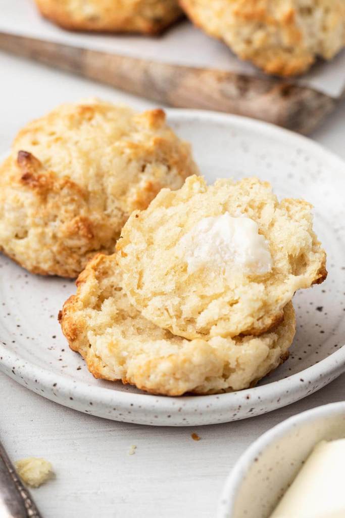 Dos galletas en un plato blanco.  Una galleta se cortó por la mitad y se cubrió con mantequilla. 