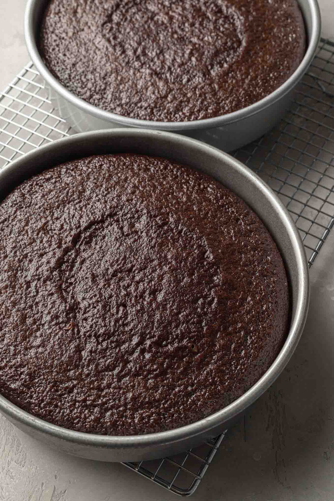 Baked chocolate cake layers in the pans sitting on a wire cooling rack.