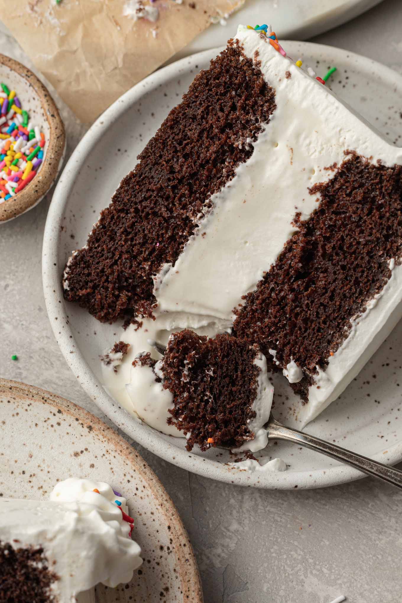 A slice of ice cream cake on a white speckled plate. A fork has cut into the cake to remove a piece.