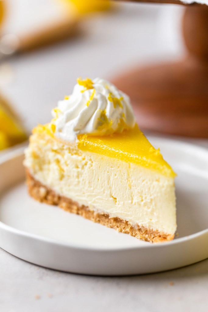 Una rebanada de tarta de queso con limón cubierta con cuajada de limón en un plato de postre blanco. 