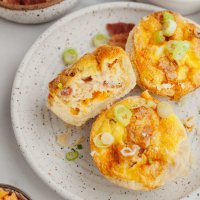 Una vista aérea de tres mini quiches en un plato blanco moteado.  Un quiche está de lado y le falta un bocado.