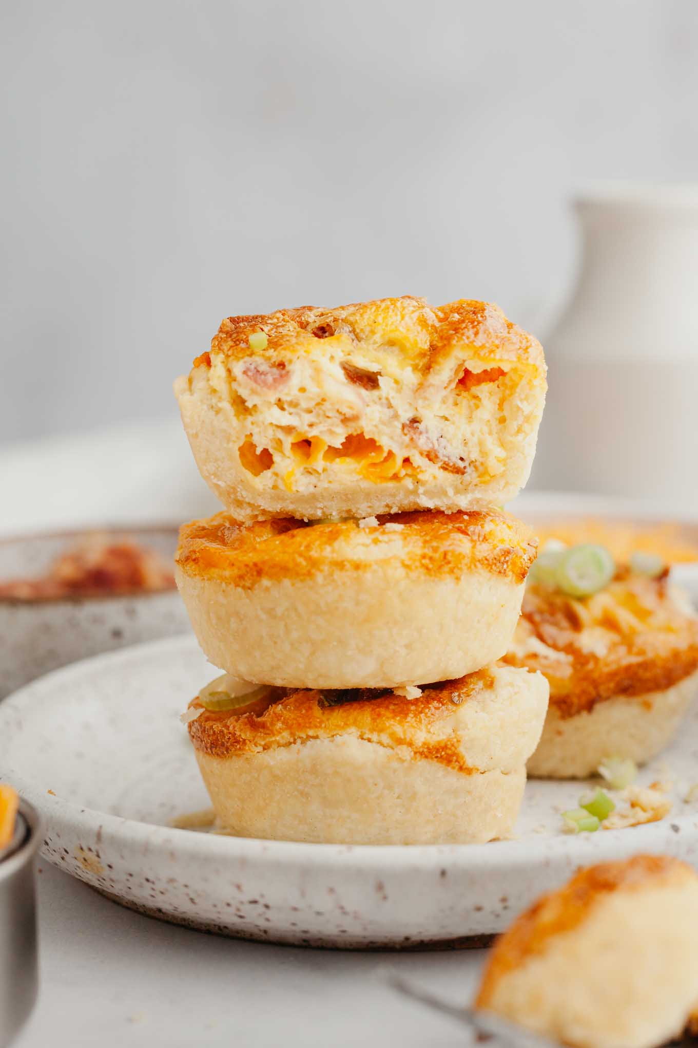 Una pila de tres quiches del tamaño de un bocado en un plato blanco moteado. 