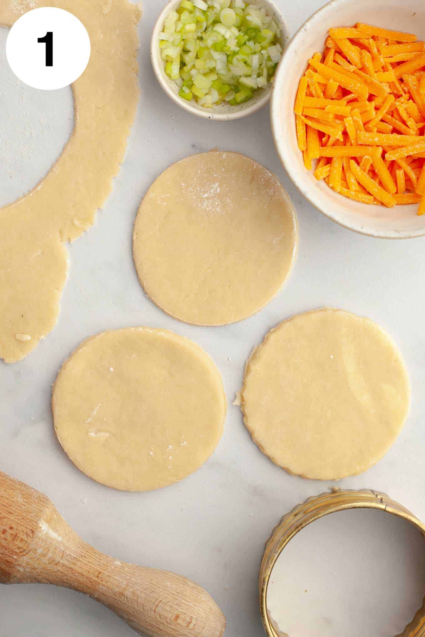 Una vista aérea de tres mini círculos de masa de tarta con ingredientes de relleno de quiche repartidos en tazones. 