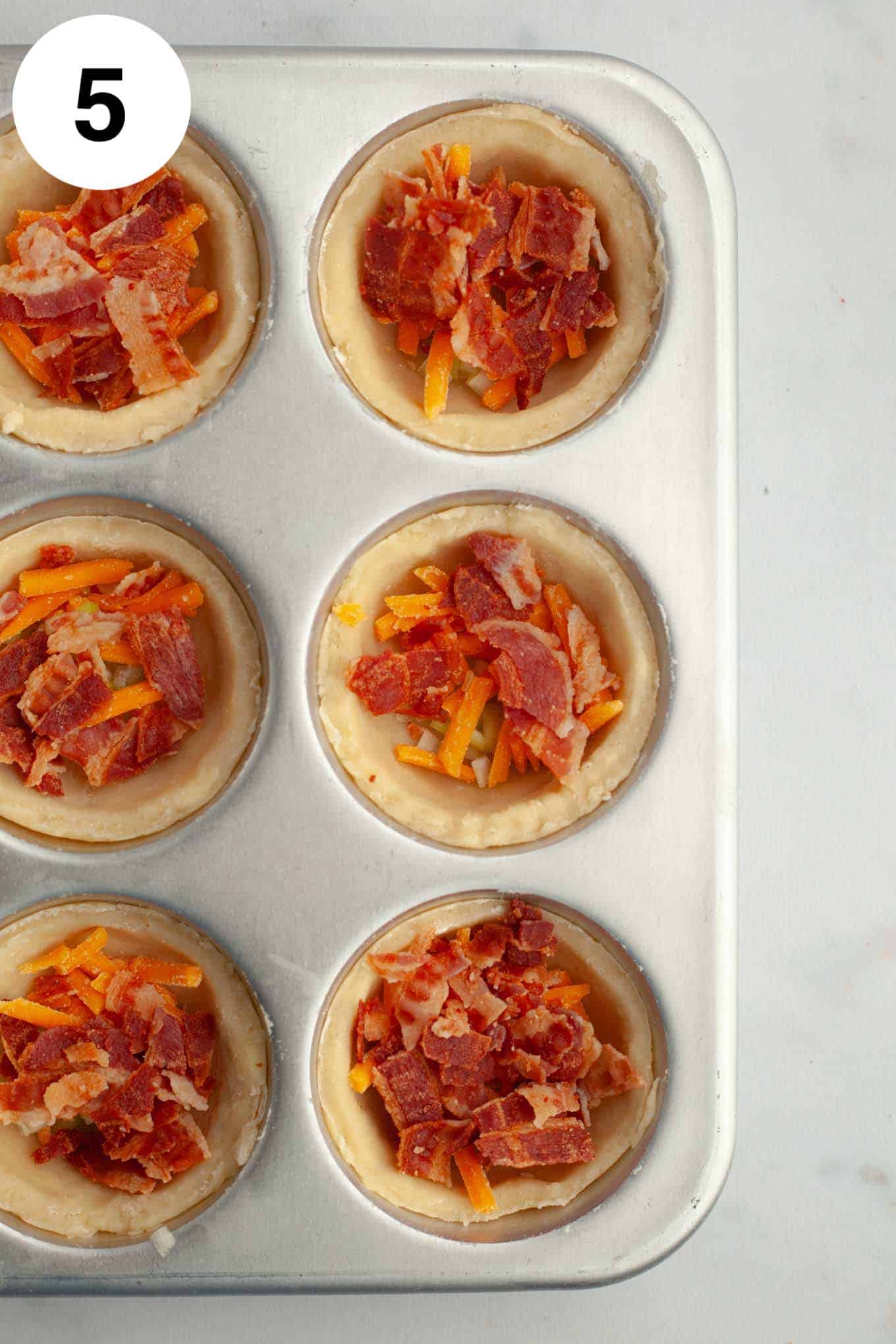 Una vista aérea de mini quiches parcialmente llenas en un molde para muffins. 