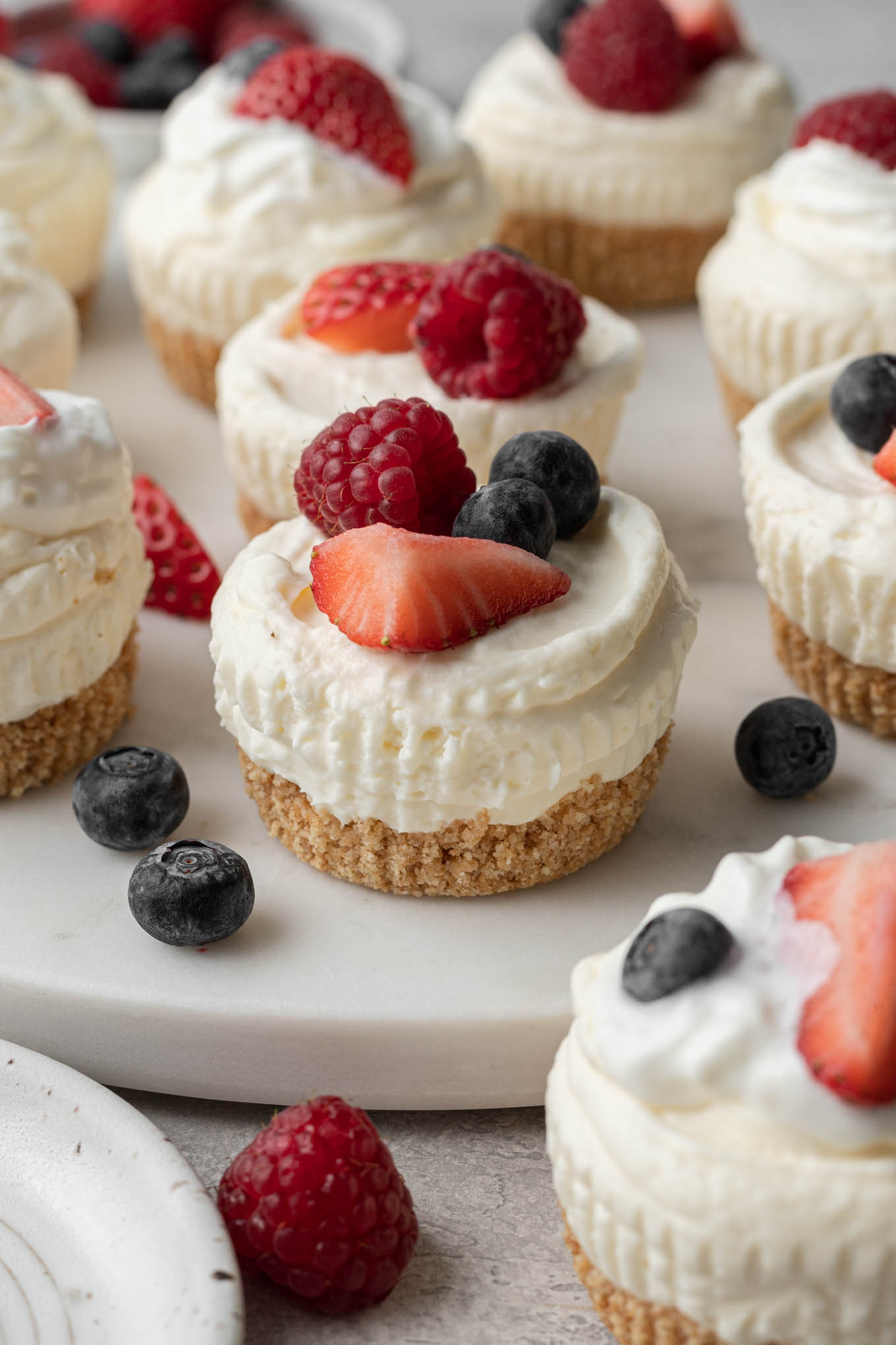 Mini cheesecakes sin hornear cubiertos con bayas frescas en un plato blanco. 