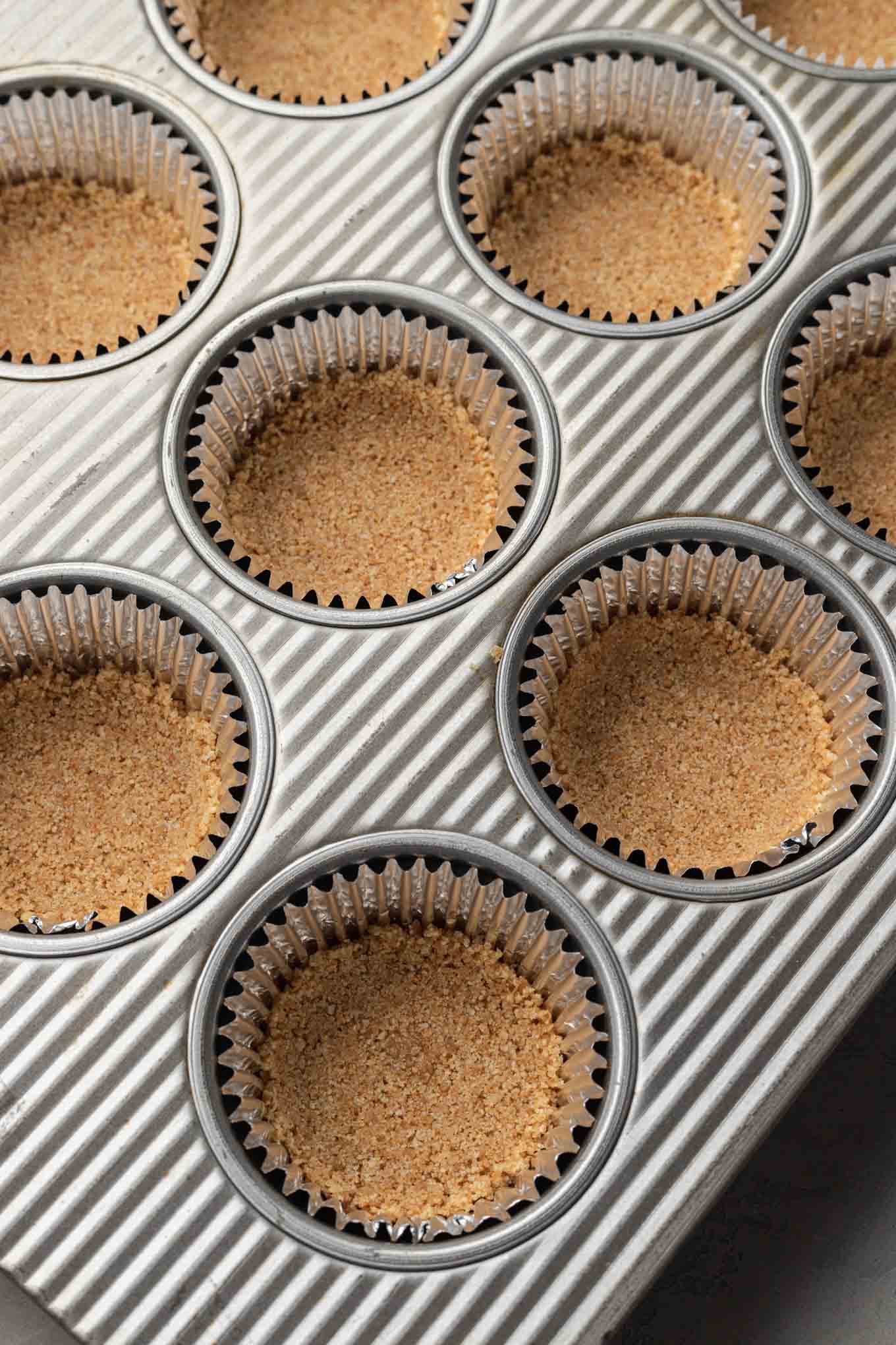 Moldes para muffins forrados con moldes para cupcakes y rellenos con una corteza de galleta Graham. 