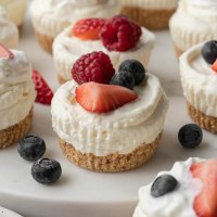 Varios mini cheesecakes sin hornear cubiertos con frutos rojos frescos.