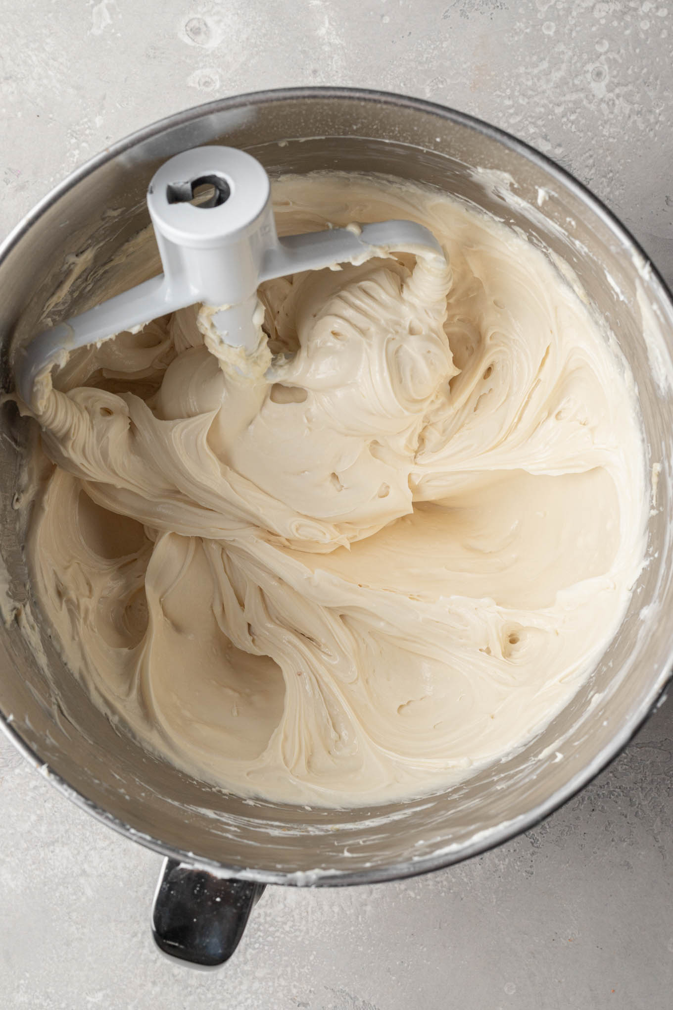 Una vista aérea de una mezcla de queso crema en el tazón de una batidora de pie, con un accesorio de paleta. 