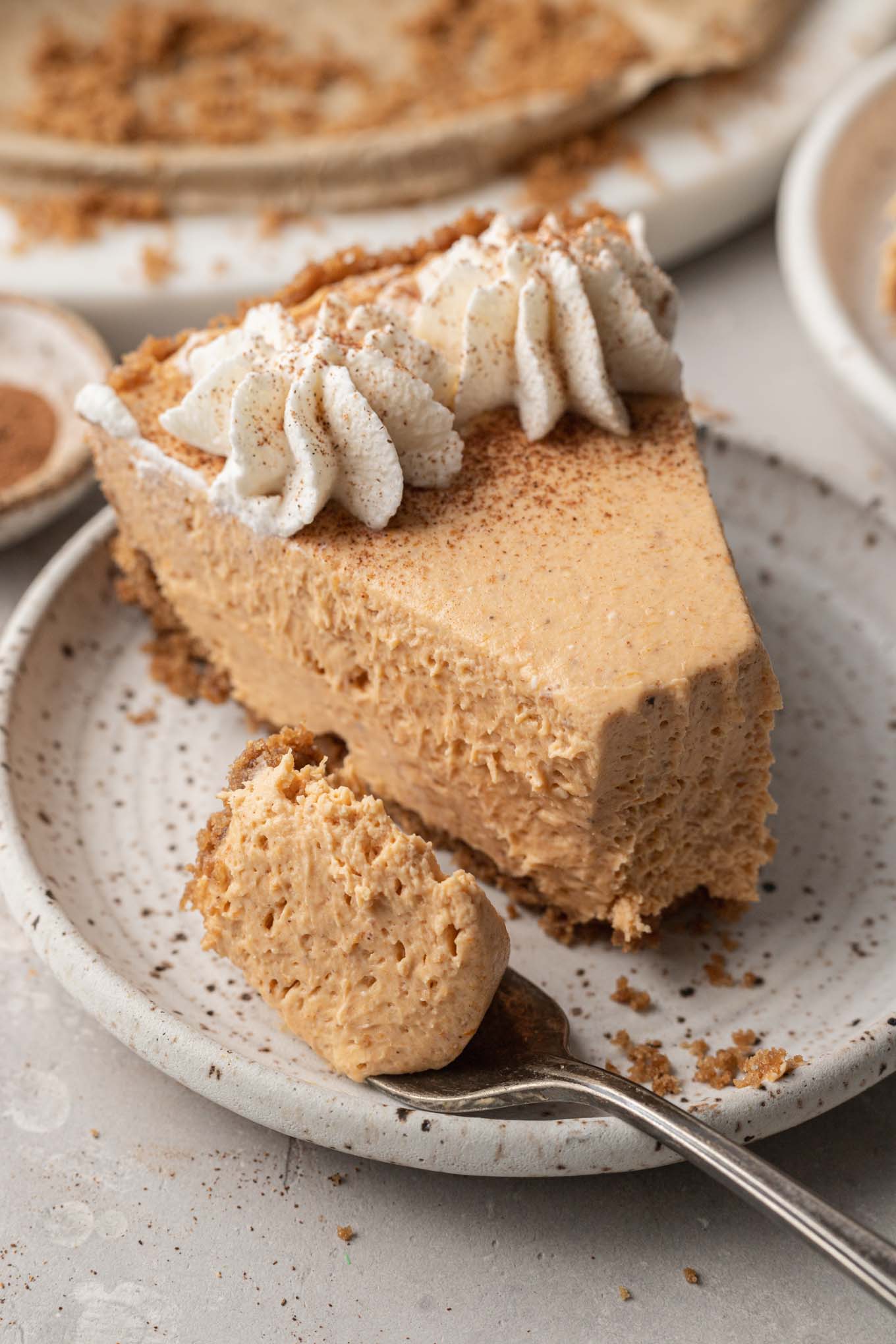 Una rebanada de tarta de queso y calabaza sin hornear en un plato de postre moteado, con un tenedor a un lado. 