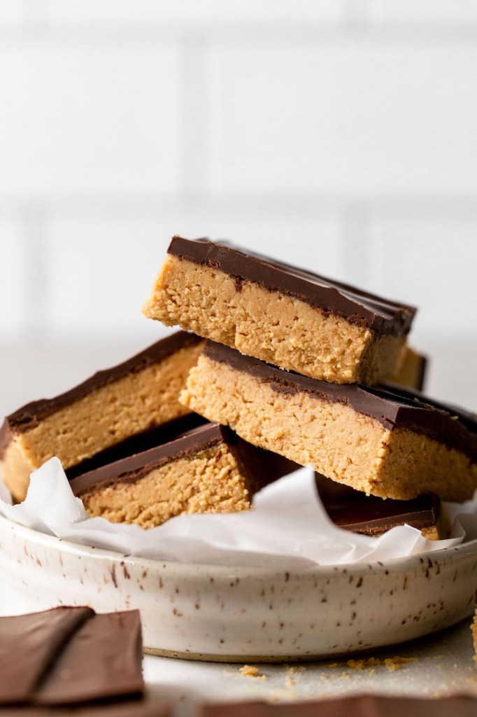 Un montón de barras de chocolate con mantequilla de maní en un plato moteado.  Más barras descansan en primer plano. 