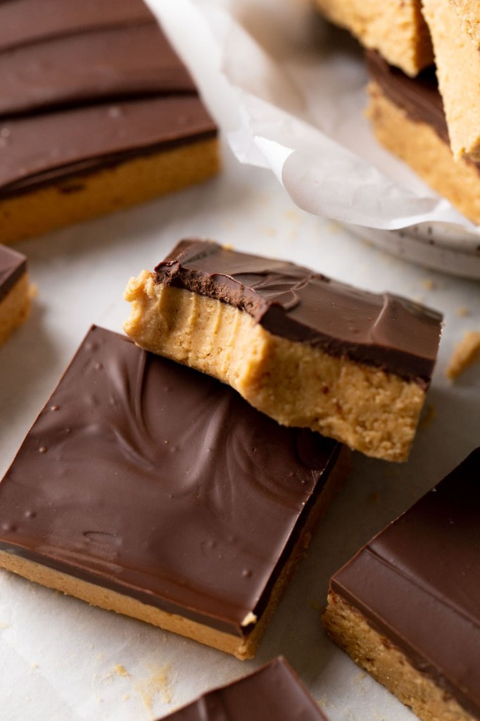 Una barra de chocolate con mantequilla de maní a la que le falta un bocado descansando encima de otra barra. 