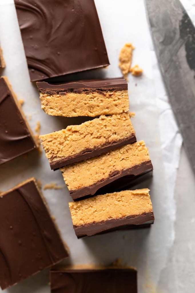 Cuatro rebanadas de barras de chocolate con mantequilla de maní, tumbadas de lado.  Los rodean barras sin cortar. 